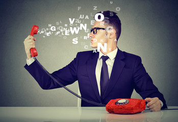 Young business man looking at telephone handset with alphabet letters flying out