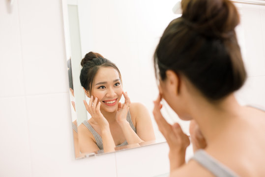 Smiling young woman looking to mirror at home bathroom