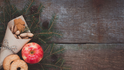 Red and yellow apple on a branch of a Christmas-tree with cookies, ginger-snaps, nuts, cones and dried cranberries. Old wooden background