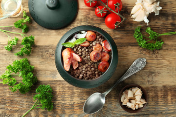 Pot with black lentils and sausages on table