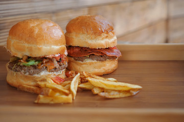 Tasty burgers with french fries on wooden tray