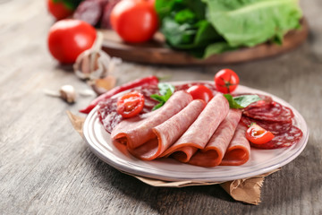 Plate with delicious sliced sausages on wooden table