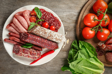 Plate with delicious sliced sausages on wooden table