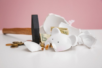 Hammer and broken piggy bank with money on white table against color background