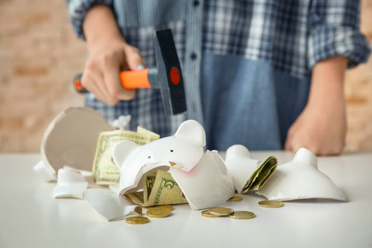 Broken piggy bank and blurred woman with hammer on background