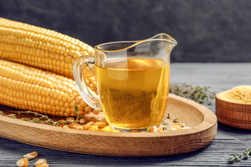 Glass pitcher with corn oil on wooden tray