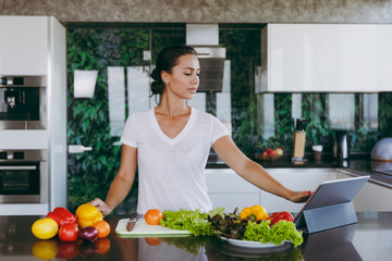 Young woman looking at recipe in laptop in kitchen. Healthy food - Vegetable salad. Diet. Dieting concept. Healthy lifestyle. Cooking at home. Prepare food. With place for text.