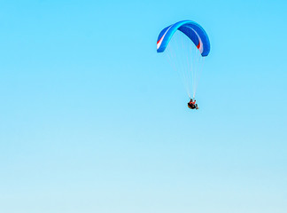 Man paragliding with blue parachute above water sea, clear sky
