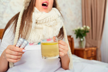 Concept of the virus is a cold disease. The girl sneezes with a mug of tea and medicines in her hand.