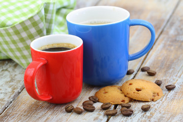 Two colorful coffee mugs and crunchy caramel biscuits on rustic wooden surface
