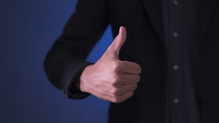 Businessman showing OK sign with his thumb up on blue and black background.