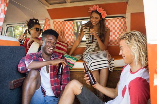 Happy friends sitting while holding beer bottles in camper van