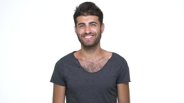slow motion handsome thin man wearing grey t-shirt looking at camera smiling broadly with white teeth posing at camera over white background. Concept of emotions