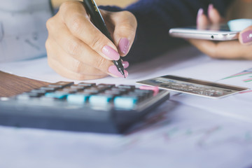 business woman hand writing and calculating her monthly expenses with
blur background credit card , another hand holding smart phone 