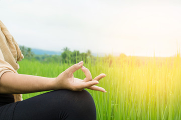 Asian woman hand doing yoga and meditation over nature green field with morning sunshine in background