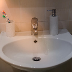 Sink in the bathroom. A cup with toothbrushes. Liquid soap.