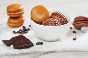 Pieces of chocolate with loose coffee beans and coffee flavored macarons in a white bowl presented on a white napkin