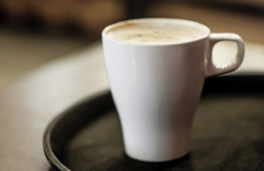 A big white ceramic cup of coffee on on a brown tray the table