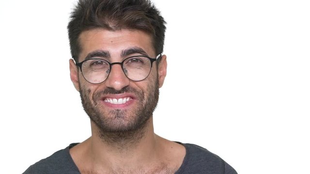 hispanic bearded guy in glasses with brilliant smile looking on camera feeling pleased over white background slow motion. Concept of emotions
