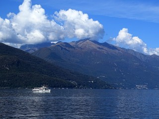 Jezioro otoczone górami, statek turystyczny na jeziorze, niebieskie niebo z malowniczymi chmurami