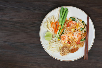 Thai fried noodle with fresh prawn on white dish on wooden table.Thai food (Pad Thai) and selective focus with space for texts.