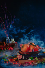 Autumn harvest still life with persimmons and figs on a stack of magical books. Dark Halloween concept with smoke. Dark food photography with copy space.