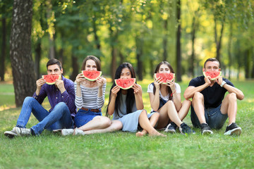 Funny men and women covering faces with tasty watermelon slices