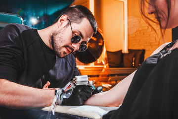 master tattooist makes a tattoo on the skin of the hand client girl in a workshop with special equipment