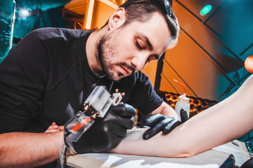 master tattooist makes a tattoo on the skin of the hand client girl in a workshop with special...
