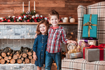 Beautiful happy laughing children in New Year interior with Christmas tree and fireplace. Brother hugging his sister. The concept of a family holiday