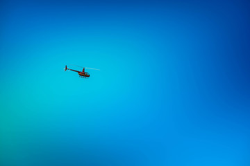 Military helicopter flying in the sky over a city and crowded event, taking photos, filming from above on clear blue sky background. An Isolated helicopter. Team of rescuers searching for lost people