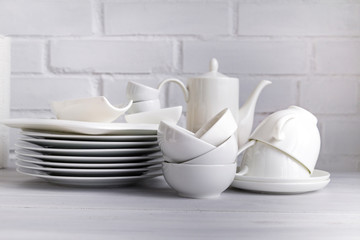 Fototapeta na wymiar White porcelain dishware stacked on a wooden table against white brick background. Concept of restaurant, cooking and service.