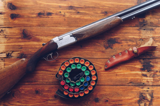 Hunting equipment. Shotgun, hunting cartridges and hunting knife on wooden table.