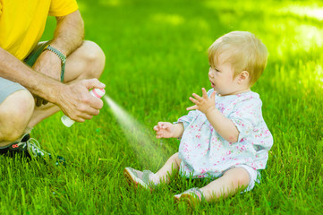 Adult man spraying insect repellents on skin baby girl - Powered by Adobe