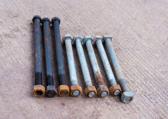 Many rusty long bolts, screw head nuts on cement ground. Close up of different size a dirty hexagon screw head nuts on concrete floor. Machine spare parts and maintenance concept. - Selective focus.