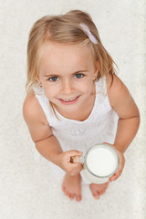 Fototapeta premium Little happy girl holding a cup of milk - top view
