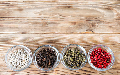 Different kinds of peppercorns.  Four variations of peppercorns in glass plates over rustic background. Black, white, green and pink pepper. Dried berries used as spice and seasoning. Food photo.