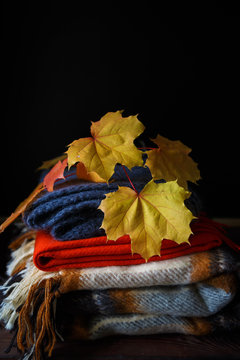 stack of warm woolen blankets of colorful in autumn style with maple leaves on a wooden background