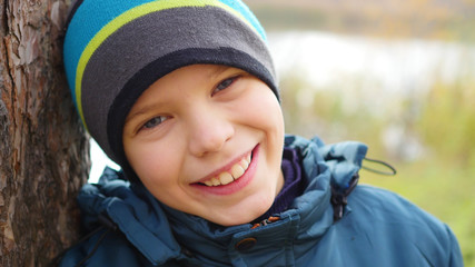 Teenager in autumn Park standing near a tree smiling and looking at camera