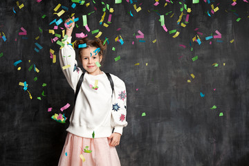 Happy child is smiling and showing a thumb up against a confetti, dressed in a pink tuxedo skirt and a white sweatshirt in a festive cap © deniskomarov