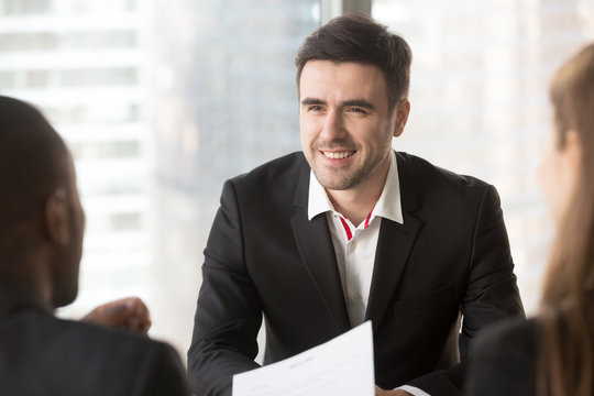 Portrait of confident job candidate talking with multinational interviewers in office, professional specialist communicating with hiring managers. Smiling businessman talking with business partners