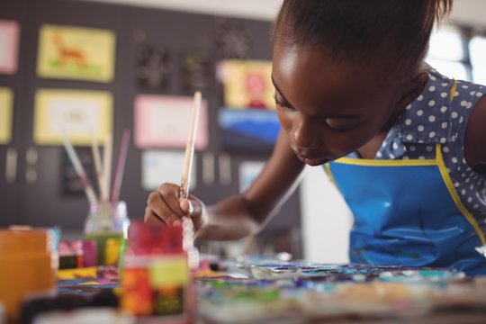 Concentrated elementary girl painting at desk