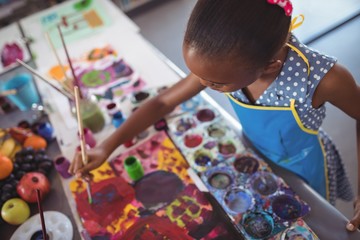 High angle view of focused elementary girl painting at desk