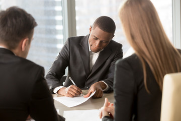 Afro american businessman putting signature on business agreement concluding deal with caucasian partners. Black job seeker singing contract, employers hiring new office worker. View over the shoulder