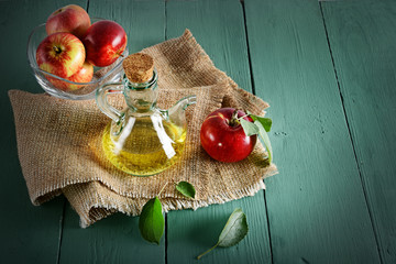 Red apples in vase and apple cider vinegar on wooden table. Concept - healthy food from your...