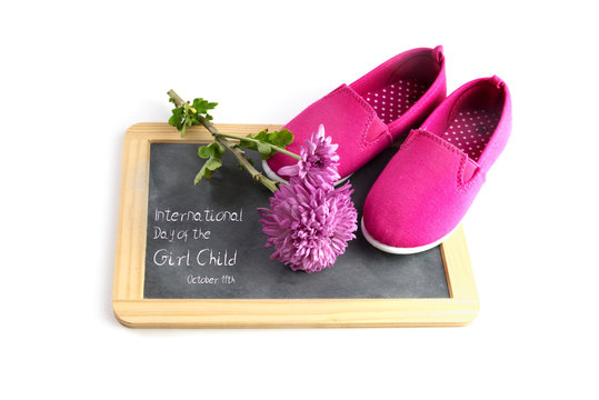 pink kid shoes and a flower on a writing blackboard isolated on a white background, text International Day of the Girl Child 11 October, copy space, selected focus
