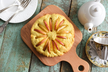 Homemade delicious rustic cake with apple slices looking like sun rays with teaware on shabby wooden blue table above view