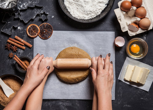 Mother with child kneading dough. Bakery ingredients, eggs, flour, butter, dried oranges and cinnamon. Raw dough on parchment paper. Christmas shapes for making cookies or gingerbreads.