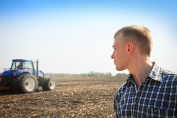 Young man in a field and a tractor on a background.