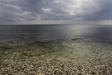 Closeup pebble stones on a beach with soft focus by the sea, waves and skyline
